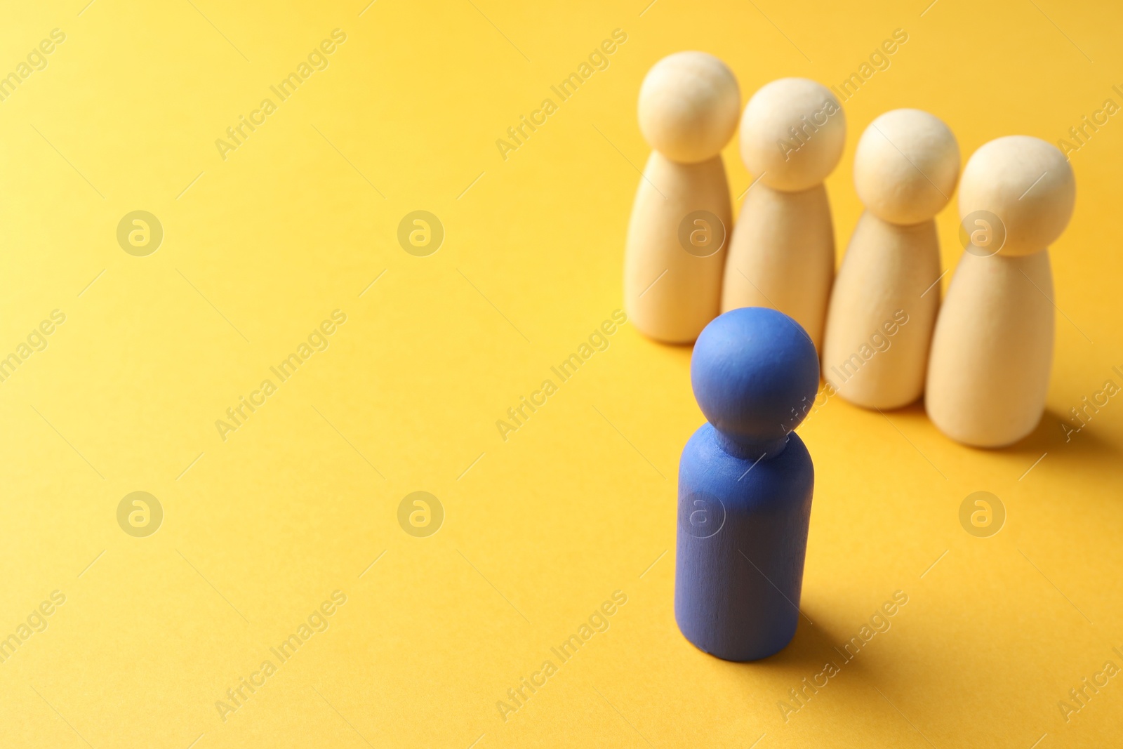 Photo of Unemployment. One blue figure among wooden on yellow background, closeup. Space for text