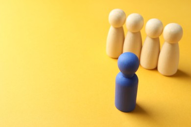 Photo of Unemployment. One blue figure among wooden on yellow background, closeup. Space for text