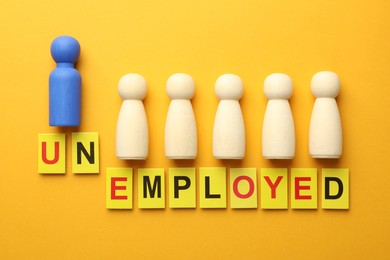 Photo of Word Unemployed and human figures on yellow background, flat lay