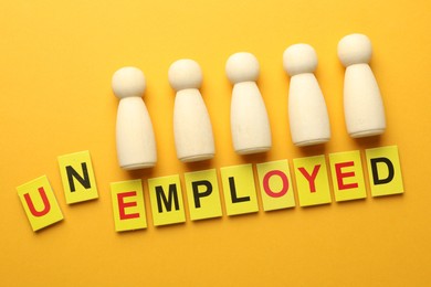 Photo of Word Unemployed and human figures on yellow background, flat lay