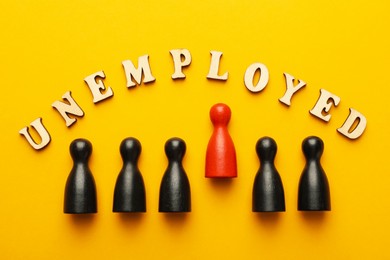 Photo of Word Unemployed and human figures on yellow background, flat lay