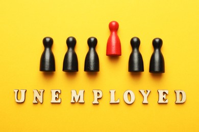 Photo of Word Unemployed and human figures on yellow background, flat lay