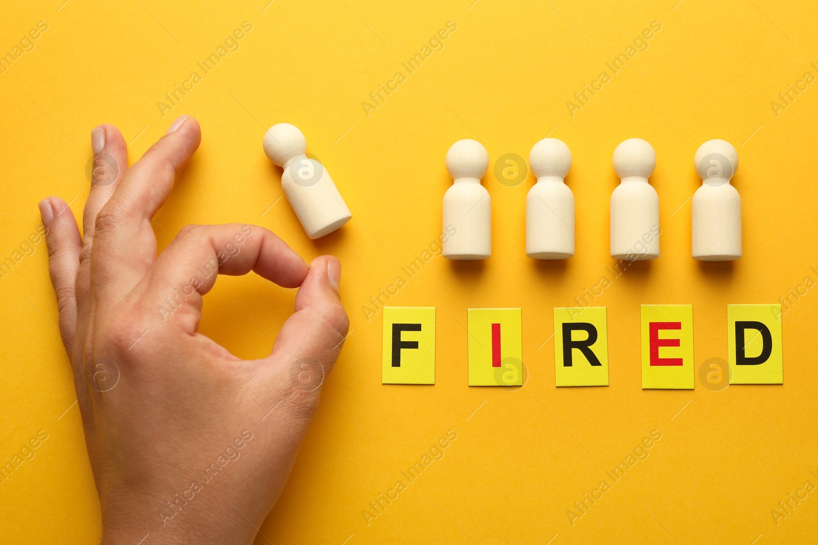 Photo of Dismissal. Word Fired and woman throwing human figure away on yellow background, top view