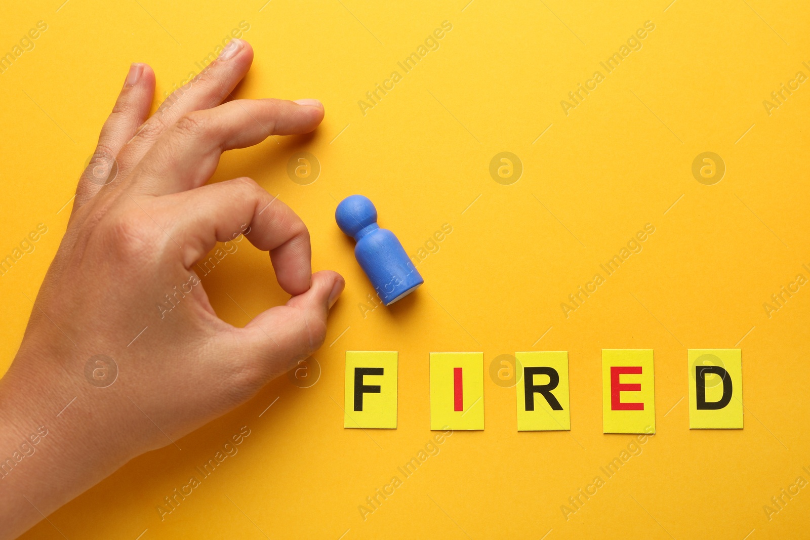 Dismissal. Word Fired and woman throwing human figure away on yellow background, top view Photo of Dismissal. Word Fired and woman throwing human figure away on yellow background, top view