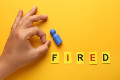 Photo of Dismissal. Word Fired and woman throwing human figure away on yellow background, top view