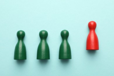 Photo of Unemployment. One red figure among green on light blue background, flat lay
