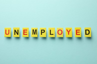 Photo of Word Unemployed on light blue background, top view