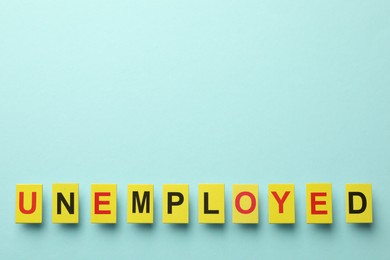 Photo of Word Unemployed on light blue background, top view. Space for text
