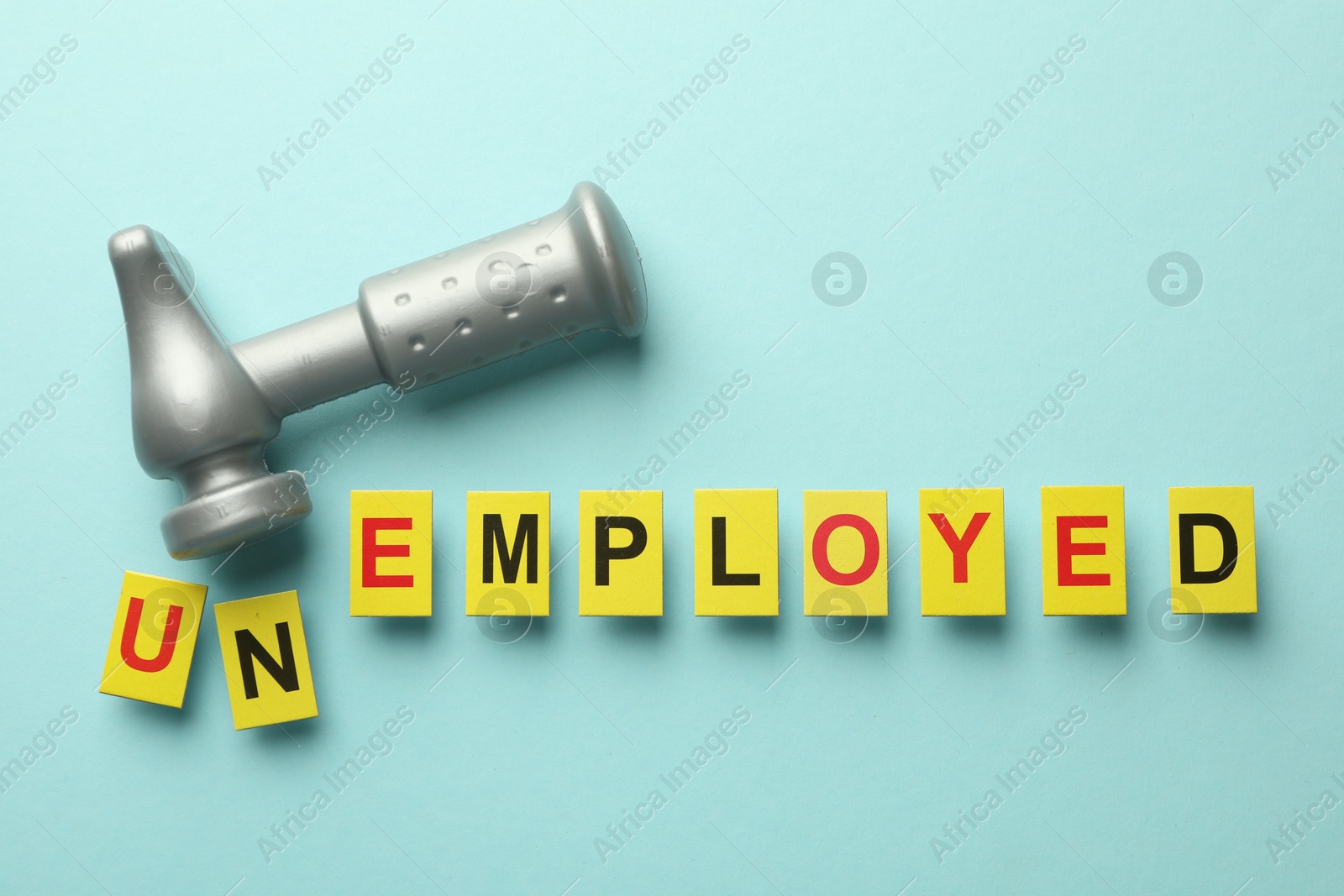 Photo of Word Unemployed and hammer on light blue background, flat lay
