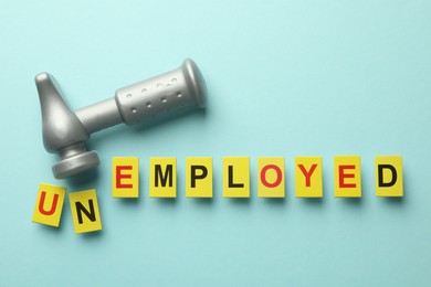 Photo of Word Unemployed and hammer on light blue background, flat lay