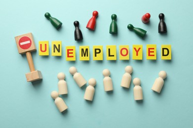 Photo of Word Unemployed, stop sign and human figures on light blue background, flat lay