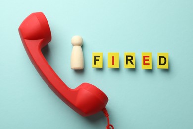 Photo of Dismissal. Word fired, telephone handle and human figure on light blue background, flat lay