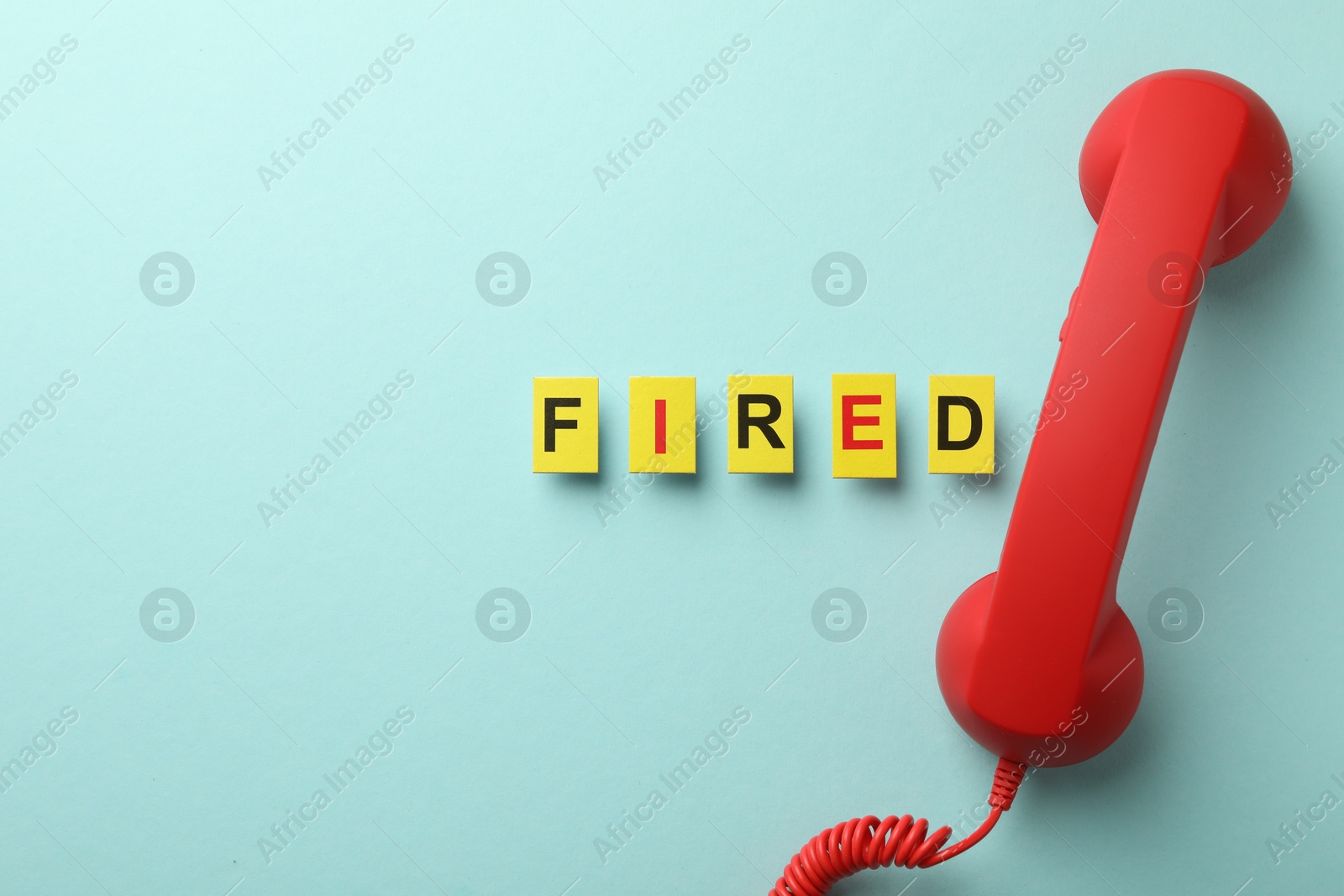 Dismissal. Word fired and telephone handle on light blue background, flat lay Photo of Dismissal. Word fired and telephone handle on light blue background, flat lay