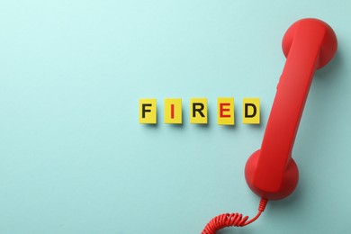 Photo of Dismissal. Word fired and telephone handle on light blue background, flat lay