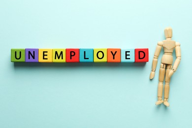 Photo of Word Unemployed and human figure on light blue background, flat lay