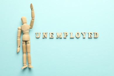 Photo of Word Unemployed and human figure on light blue background, flat lay