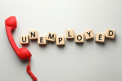 Photo of Word Unemployed and telephone handle on light background, flat lay