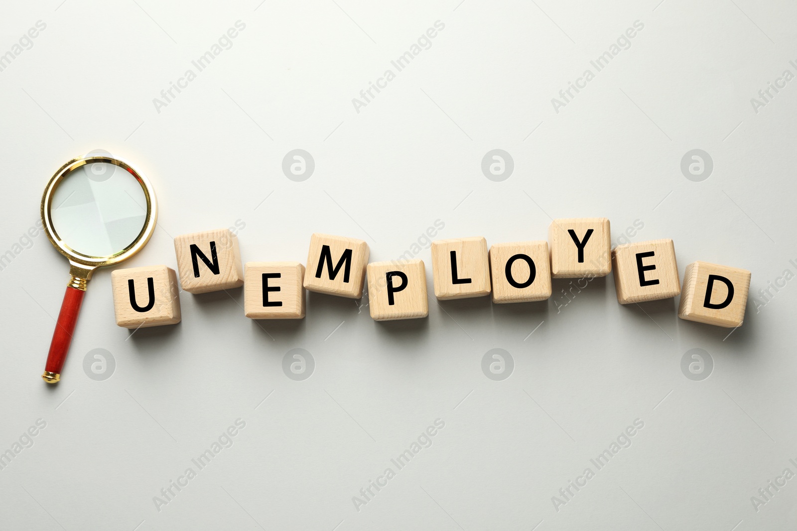 Photo of Word Unemployed and magnifying glass on light background, flat lay