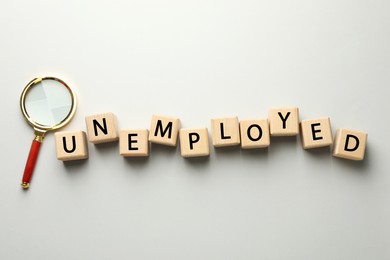 Photo of Word Unemployed and magnifying glass on light background, flat lay