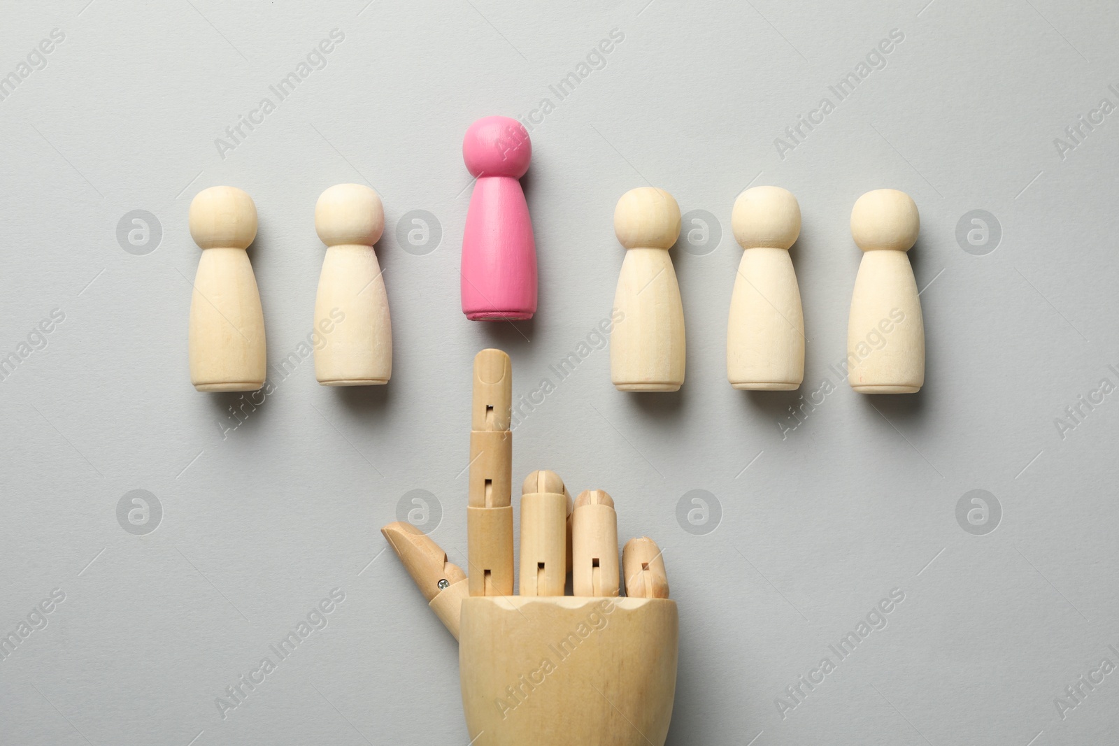 Photo of Unemployment. Hand figure pointing at pink figure among wooden on light background, flat lay