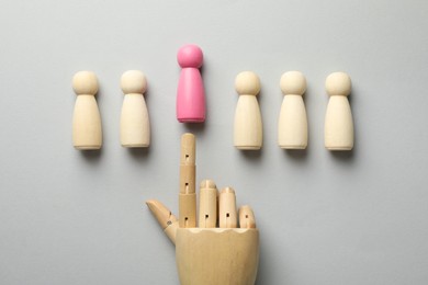 Photo of Unemployment. Hand figure pointing at pink figure among wooden on light background, flat lay
