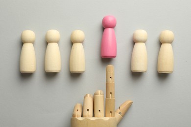 Photo of Unemployment. Hand figure pointing at pink figure among wooden on light background, flat lay