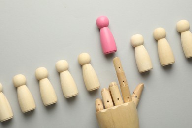 Photo of Unemployment. Hand figure pointing at pink figure among wooden on light background, flat lay