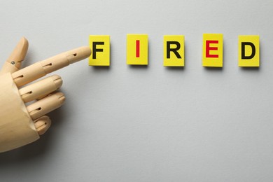Photo of Dismissal. Word fired and hand figure on light background, top view