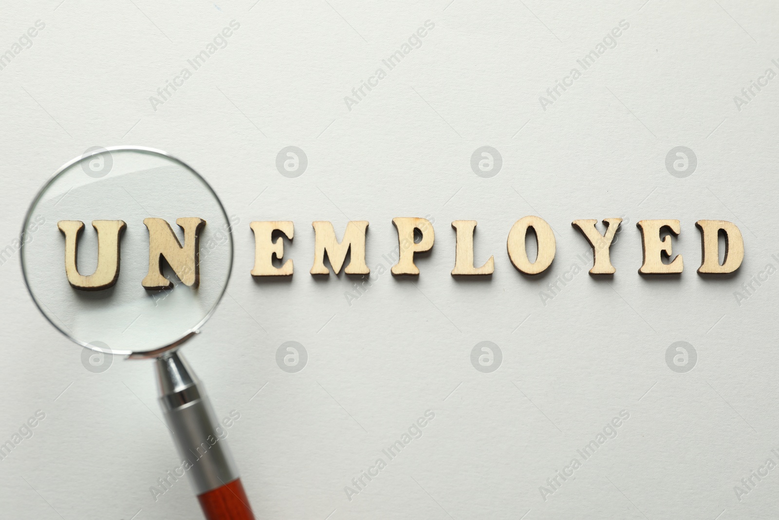 Photo of Word Unemployed and magnifying glass on light background, flat lay