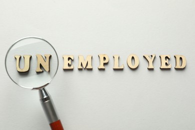 Photo of Word Unemployed and magnifying glass on light background, flat lay