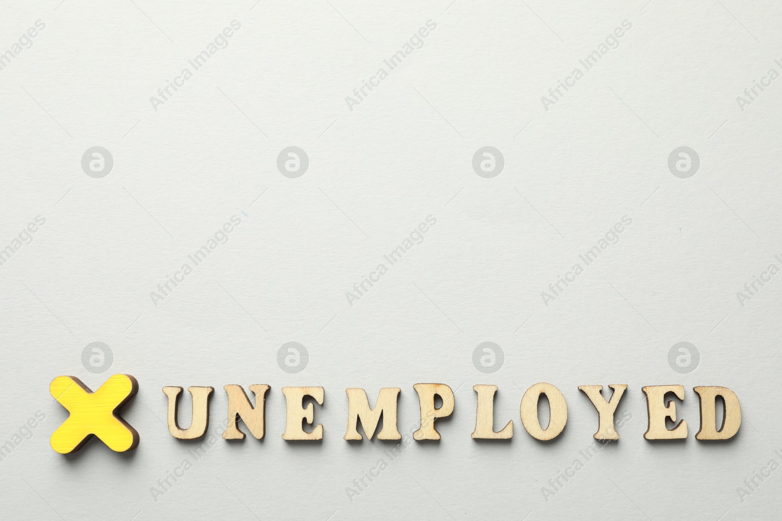 Photo of Word Unemployed and cross on light background, flat lay. Space for text
