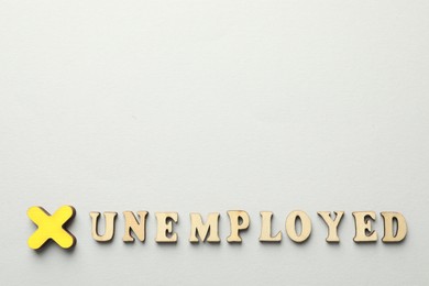 Photo of Word Unemployed and cross on light background, flat lay. Space for text