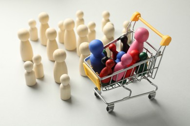 Photo of Unemployment. Many different human figures and mini cart on light background, closeup