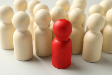 Photo of Unemployment. One red figure among wooden on light background, closeup