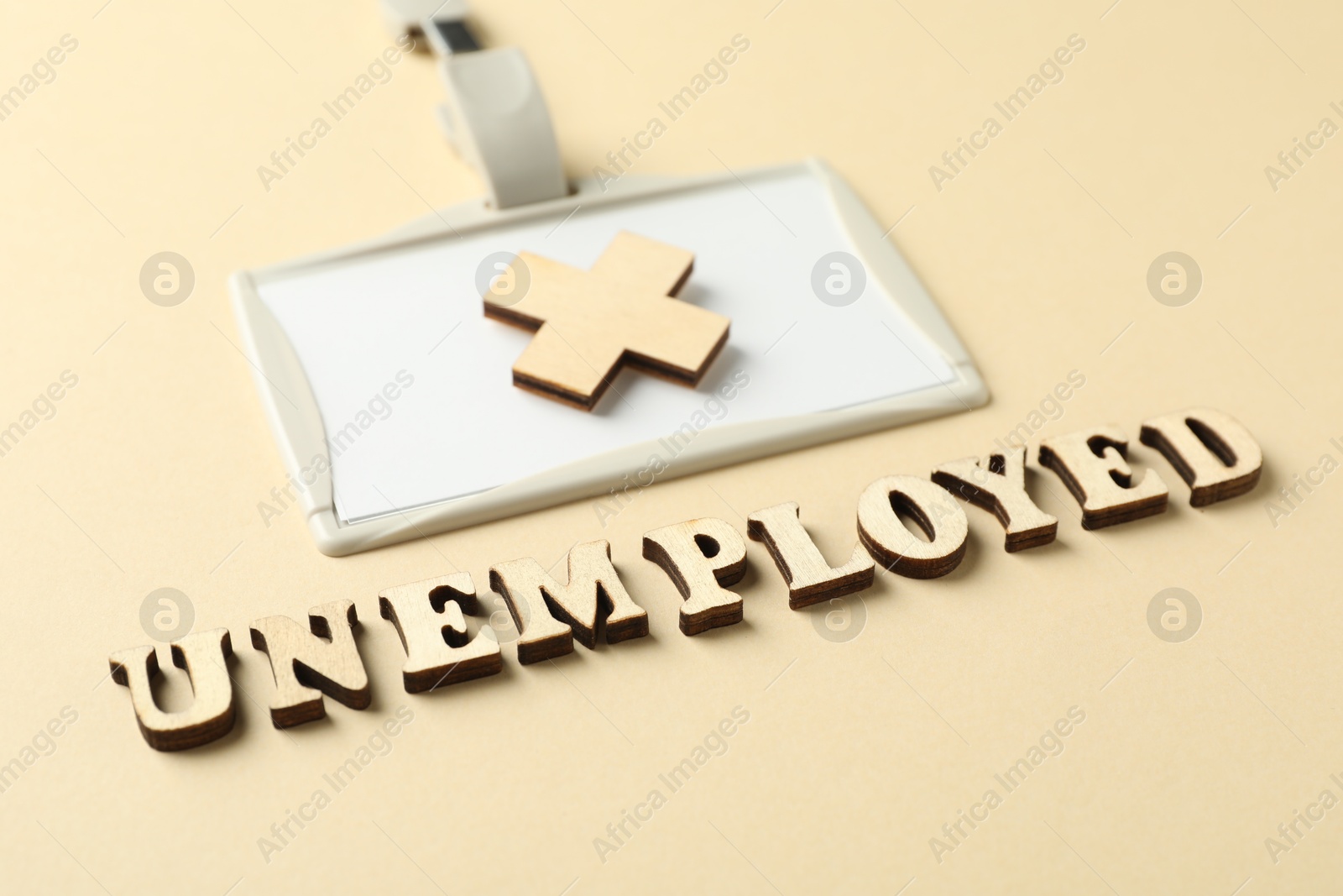 Photo of Word Unemployed, badge and cross on beige background, closeup