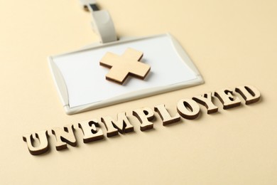 Photo of Word Unemployed, badge and cross on beige background, closeup