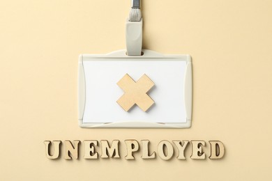 Photo of Word Unemployed, badge and cross on beige background, flat lay