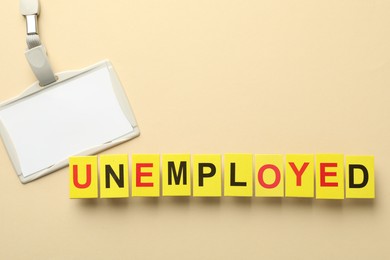 Photo of Word Unemployed and badge on beige background, flat lay