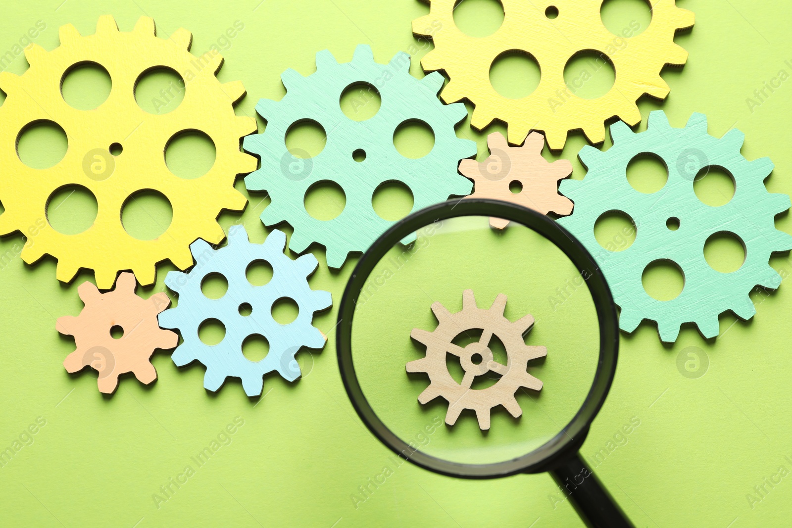 Photo of Unemployment. Gearwheels and magnifying glass on green background, flat lay