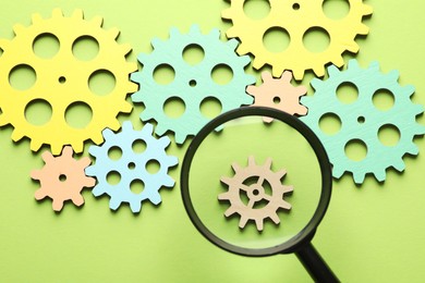 Photo of Unemployment. Gearwheels and magnifying glass on green background, flat lay