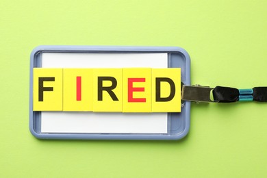 Photo of Dismissal. Word fired and badge on green background, top view