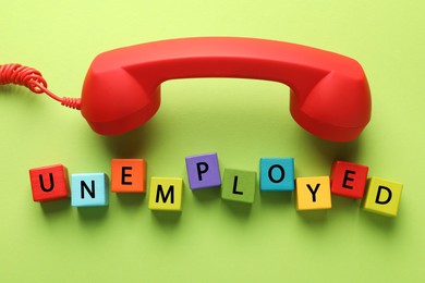 Photo of Word Unemployed and telephone handle on green background, flat lay