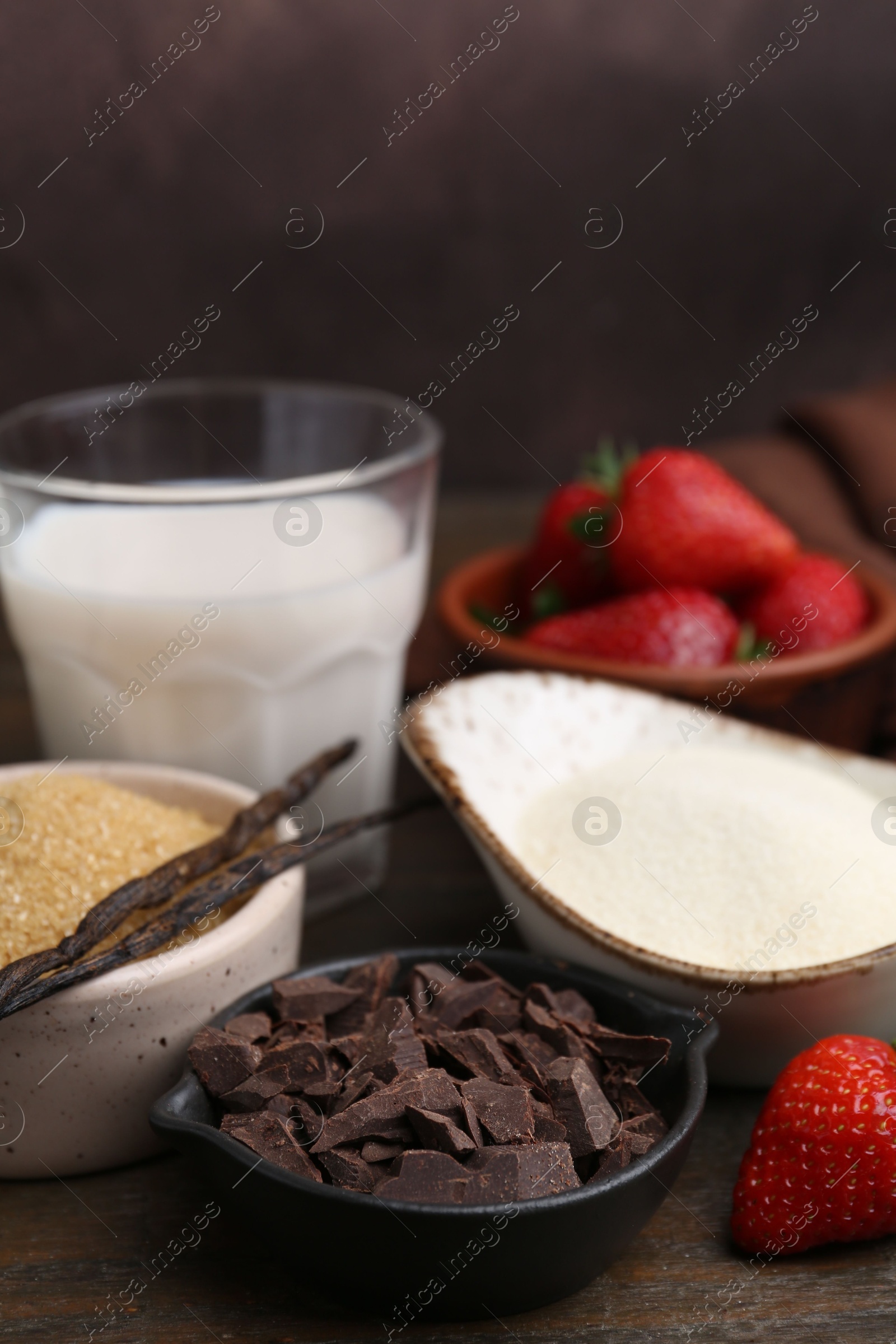 Photo of Different ingredients for panna cotta. Milk, sugar, vanilla, chocolate and strawberries on wooden table, closeup