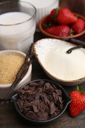 Photo of Different ingredients for panna cotta. Milk, sugar, vanilla, chocolate and strawberries on wooden table, closeup