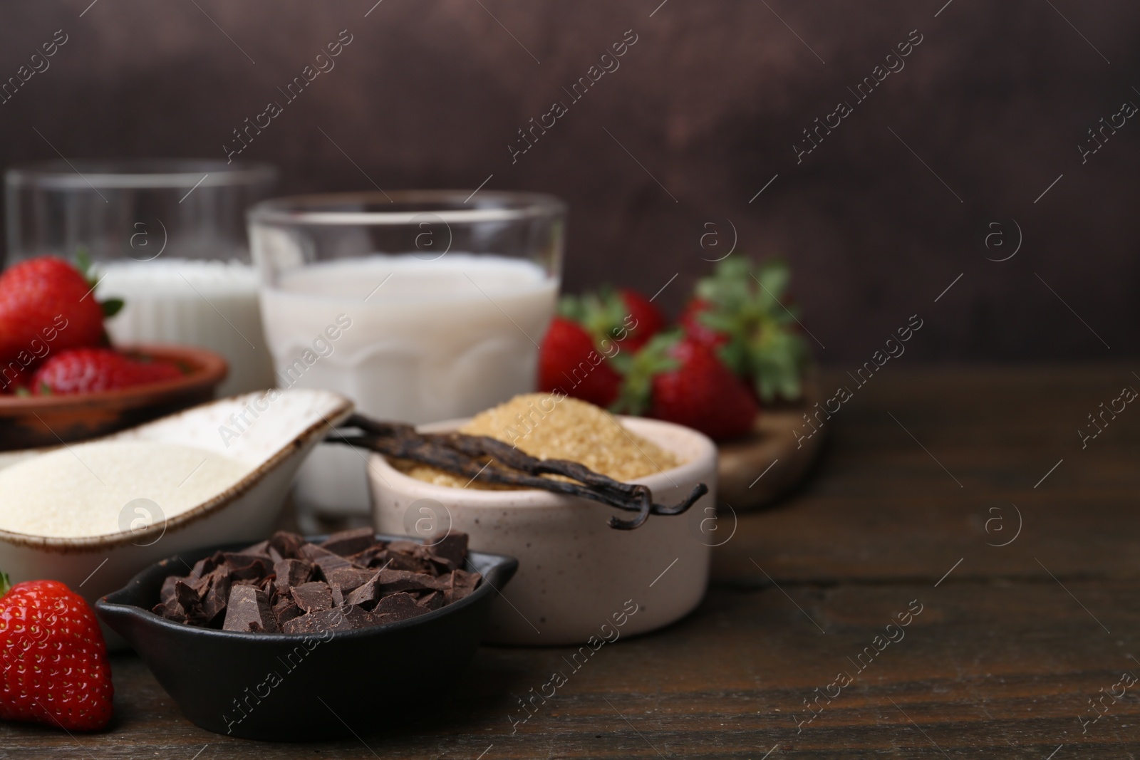 Photo of Different ingredients for panna cotta. Milk, sugar, vanilla, chocolate and strawberries on wooden table, closeup. Space for text