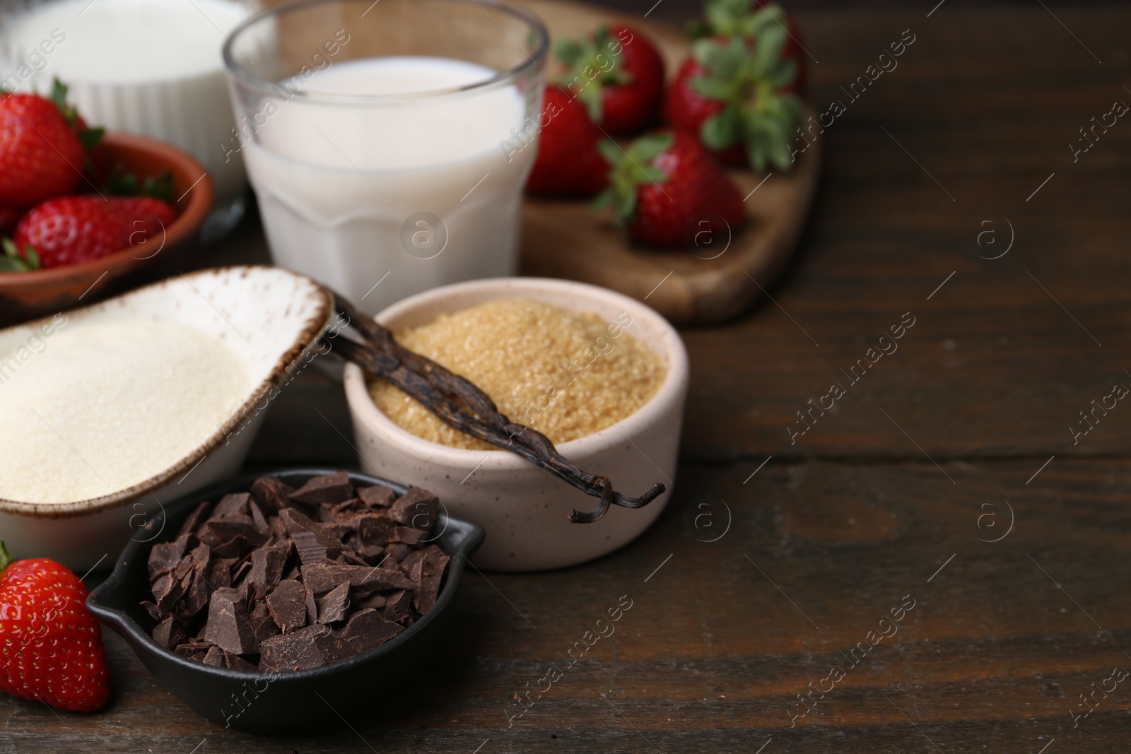 Photo of Different ingredients for panna cotta. Milk, sugar, vanilla, chocolate and strawberries on wooden table, closeup. Space for text