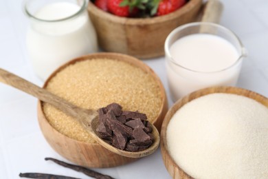 Photo of Different ingredients for panna cotta. Milk, sugar, vanilla, chocolate and strawberries on white tiled table, closeup