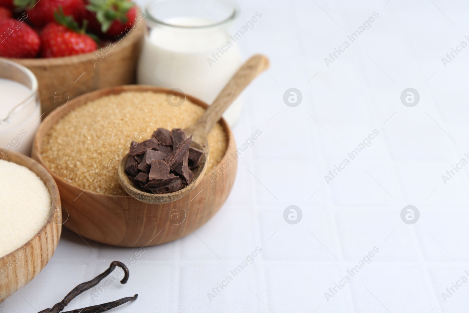 Photo of Different ingredients for panna cotta. Milk, sugar, vanilla, chocolate and strawberries on white tiled table, closeup. Space for text