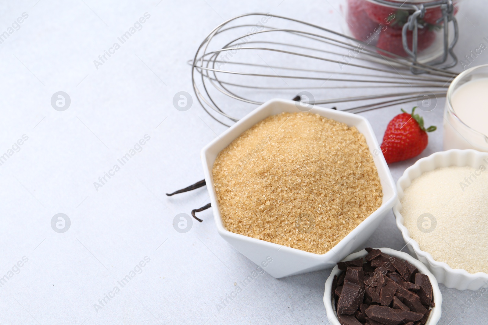 Photo of Different ingredients for panna cotta. Milk, sugar, vanilla, chocolate and strawberries on white table, closeup. Space for text