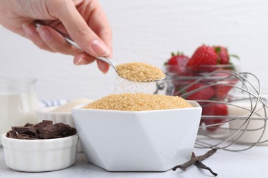 Photo of Making tasty panna cotta. Woman taking sugar with spoon at white table, closeup
